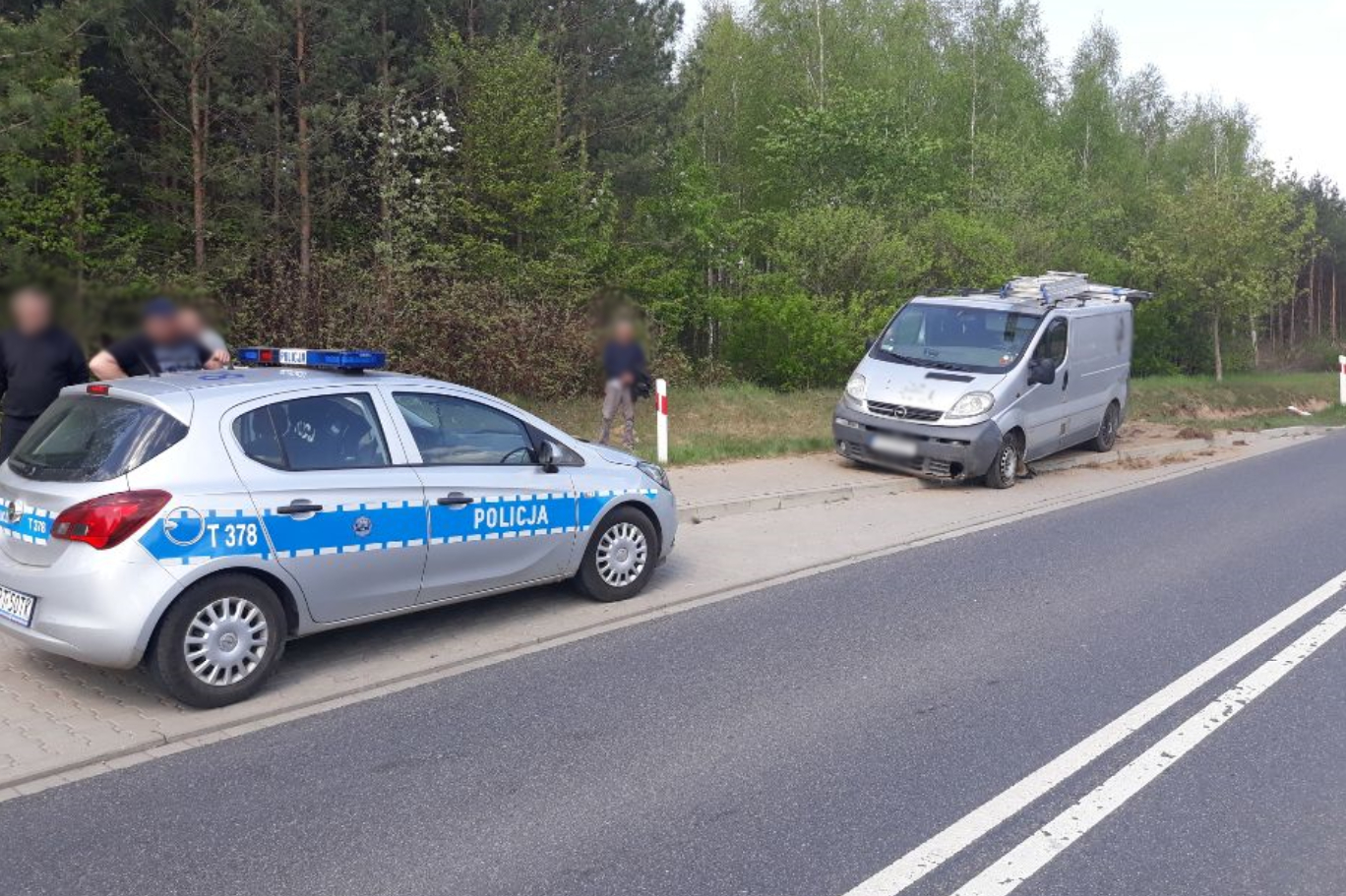 Na poboczu drogi stoi policyjny oznakowany radiowóz marki Opel oraz uszkodzony dostawczy opel koloru srebrnego