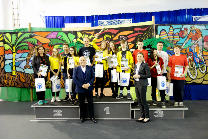 Grupowe zdjęcie na podium stoją 3 zwycięskie drużyny pośród szkół gimnazjalnych