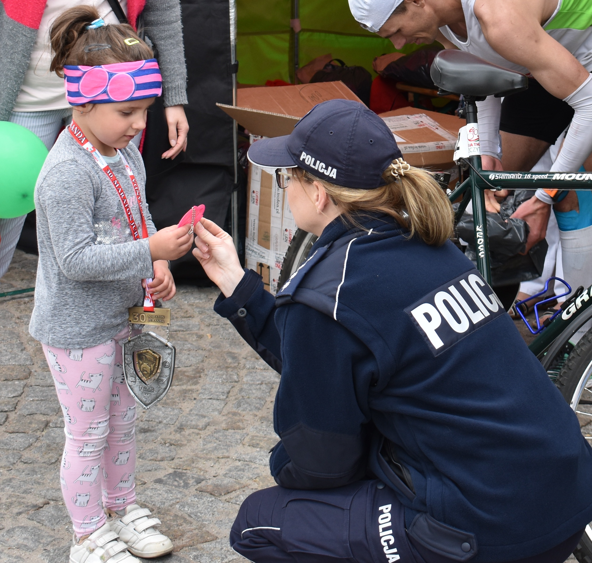 Policjantka wręcza odblask kilkuletniej dziewczynce, która przyszła odwiedzić policyjne stanowisko podczas 30 Maratonu Juranda