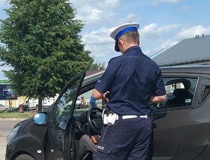 Umundurowany policjant stoi przy samochodzie i przeprowadza kontrolę drogową