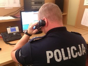 Policjant siedzący przy biurku trzymający w ręku słuchawkę telefonu
