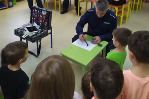 Policjant prezentujący przedszkolakom jak ściąga odciski palców z białej kartki