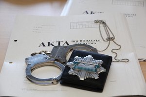 Kajdanki i policyjna odznaka leżące na teczce z aktami