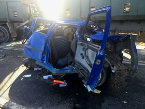 Rozbity samochód osobowy stojący na drodze obok ciężarówek, w które uderzył.