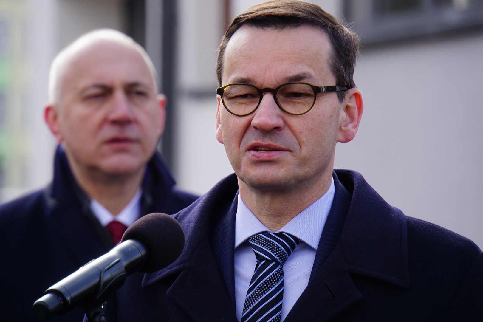 Premier Mateusz Morawiecki przemawia przed budynkiem posterunku, w tle minister Joachim Brudziński