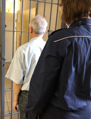 Policjant i zatrzymany 50-letni mężczyzna stojący przed pomieszczeniem dla osób zatrzymanych