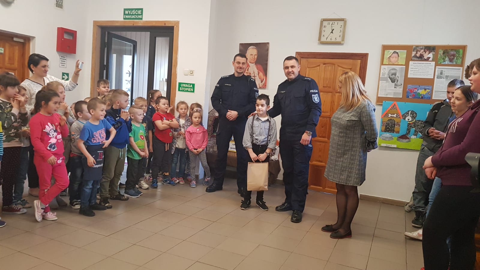 Komendant Powiatowy Policji w Braniewie z uczniami SP w Lipowinie. Komendant wręcza upominek wyróżnionemu uczniowi