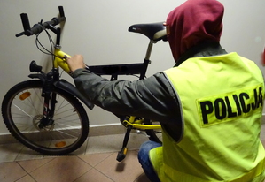 Policjant w zielonej kamizelce z napisem Policja i odzyskany rower koloru czarno żółtego