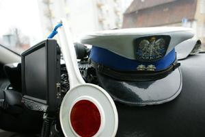 Na podszybiu policyjnego radiowozu znajduje się czapka policjanta ruchu drogowego i tarczka do zatrzymywania pojazdów