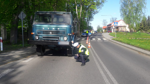Samochód ciężarowy stojący na drodze  i kucający przy nim policjant