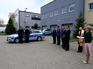 Stojące przed budynkiem komendy osoby biorące udział w przekazaniu radiowozu i radiowóz.