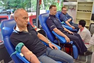 Trzy osoby, w tym umundurowany policjant na przygotowanych stanowiskach oddają krew