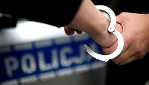 Kajdanki zakładane na rękę, w tle napis Policja na drzwiach radiowozu