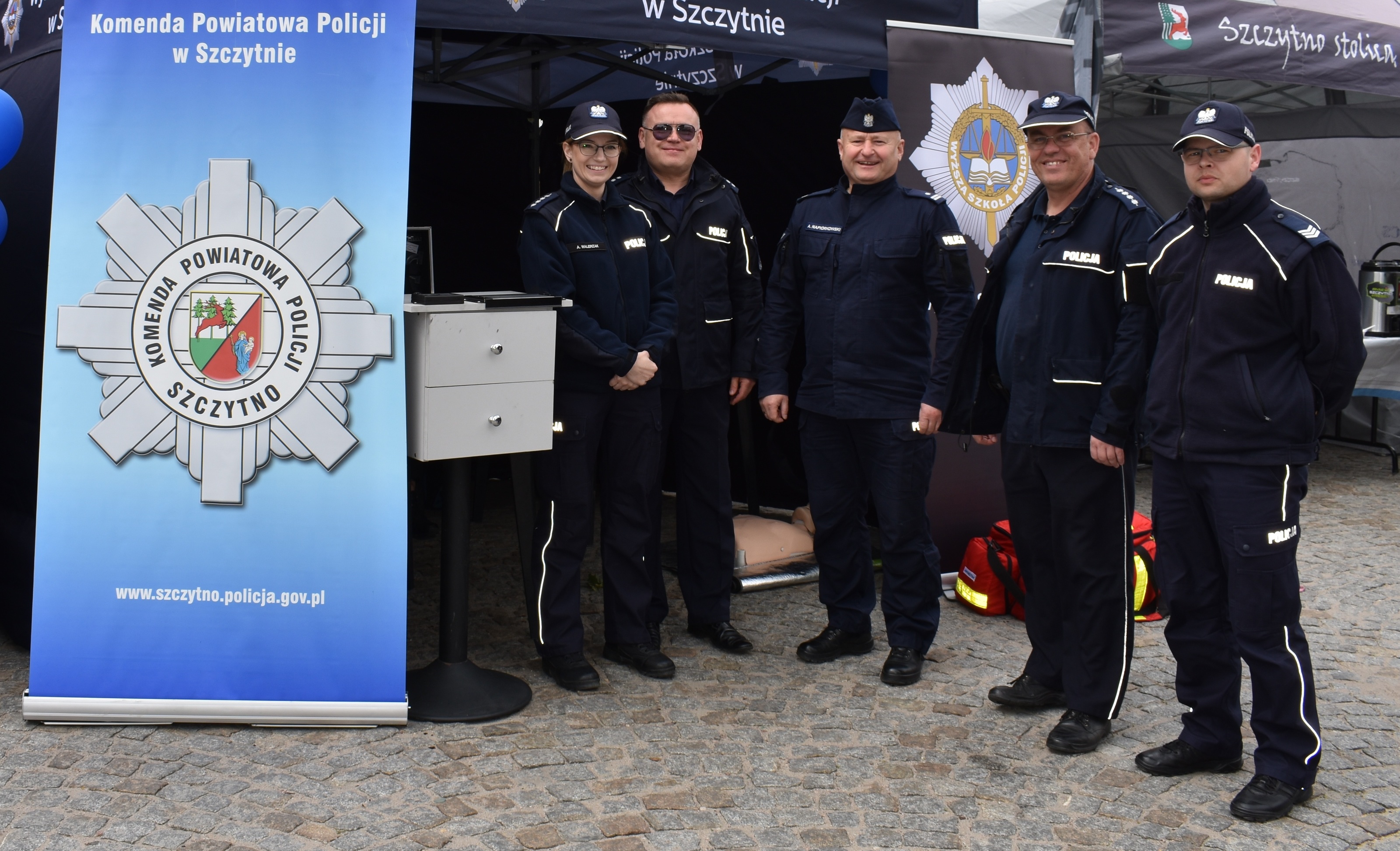 Grupowe zdjęcie policjantów na policyjnym stoisku podczas 30 Maratonu Juranda. Są to funkcjonariusze z KPP Szczytno oraz Wspol-u