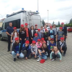 Zdjęcie grupowe dzieci z policjantem. W tle widoczny radiowóz