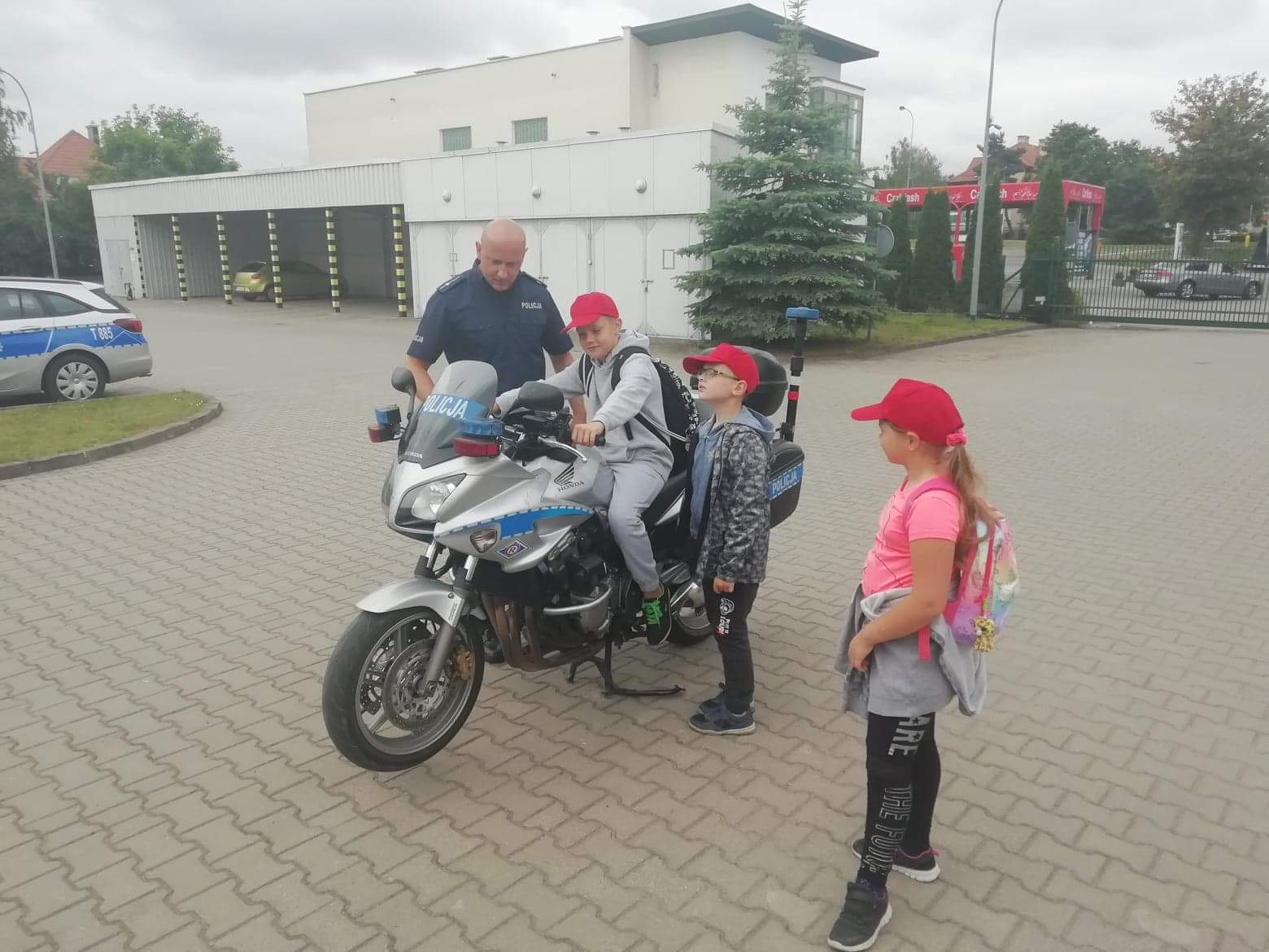 Dzieci wraz z funkcjonariuszem oglądają policyjny motocykl