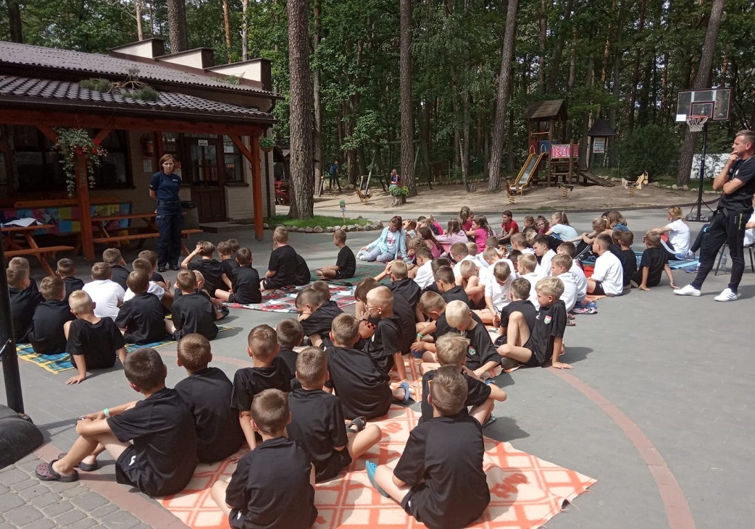 Policjantka stoi przed grupą dzieci i przypomina o bezpiecznych zachowaniach nad wodą