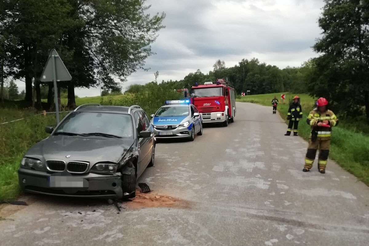Miejsce zdarzenia drogowego w powiecie gołdapskim. Uszkodzony samochód na poboczu, a za nim radiowóz i wóz strażacki