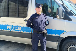 Na zdjęciu znajduje się umundurowany policjant, w tle znajduje się radiowóz.