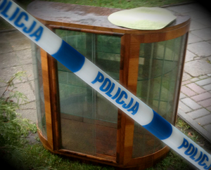 Odzyskana drewniana z elementami szklanymi komoda, na pierwszym planie biało- niebieska taśma z napisem policja