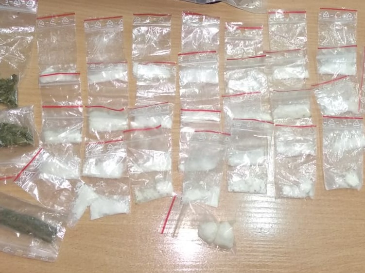 Na stole znajduje się kilkanaście woreczków foliowych z białym proszkiem i kilka z zielonym suszem
