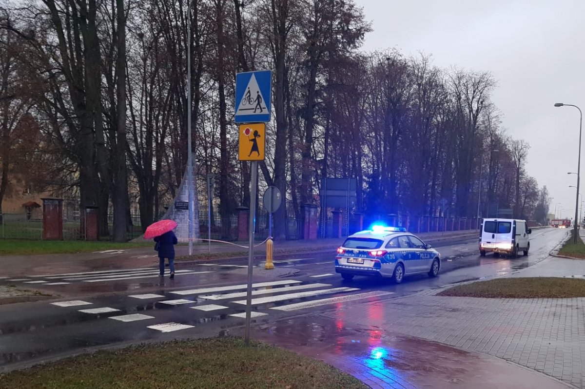 Miejsce potrącenia pieszego w Bartoszycach. Jezdnia, przejście dla pieszych, radiowóz  i uszkodzony samochód stojący na jezdni