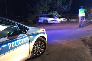 Miejsce wypadku drogowego w miejscowości Płozy. Na pierwszym planie radiowóz, a dalej policjant obok rozbitego samochodu