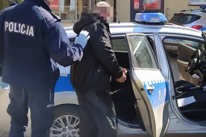 Zatrzymany mężczyzna prowadzony przez policjanta do radiowozu