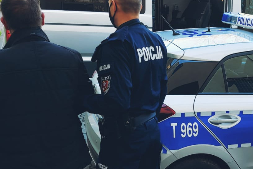 Zatrzymany mężczyzna prowadzony przez policjanta do radiowozu