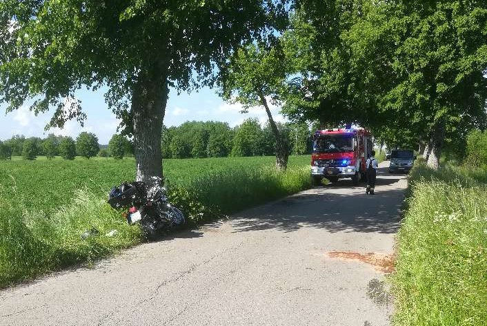 Miejsce zdarzenia drogowego w powiecie węgorzewskim. Uszkodzony motocykl na poboczu drogi, w tle wóz strażacki