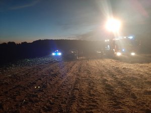 Miejsce wypadku z udziałem paralotniarza. Samochody służb ratunkowych z włączonymi światłami, stojące na polu