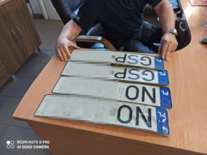 cztery tablice rejestracyjne leżą na biurku, jedną z nich trzyma policjant w rękach.