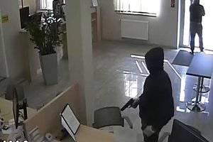 Zrzut ekranu z nagrania monitoringu. Napastnik z przedmiotem przypominającym broń w ręku we wnętrzu placówki bankowej.