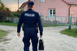 Dzielnicowy podczas obchodu rejonu służbowego, w ręku trzyma aktówkę, drogą gruntową idzie w kierunku domu jednorodzinnego