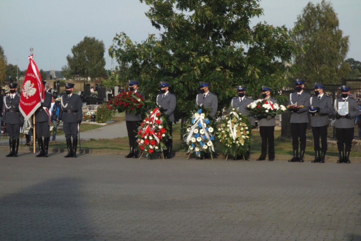 Policjanci stojący w szeregu z wieńcami pogrzebowymi