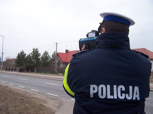 Policjant stojący tyłem w ręku trzyma urządzenie do pomiaru prędkości
