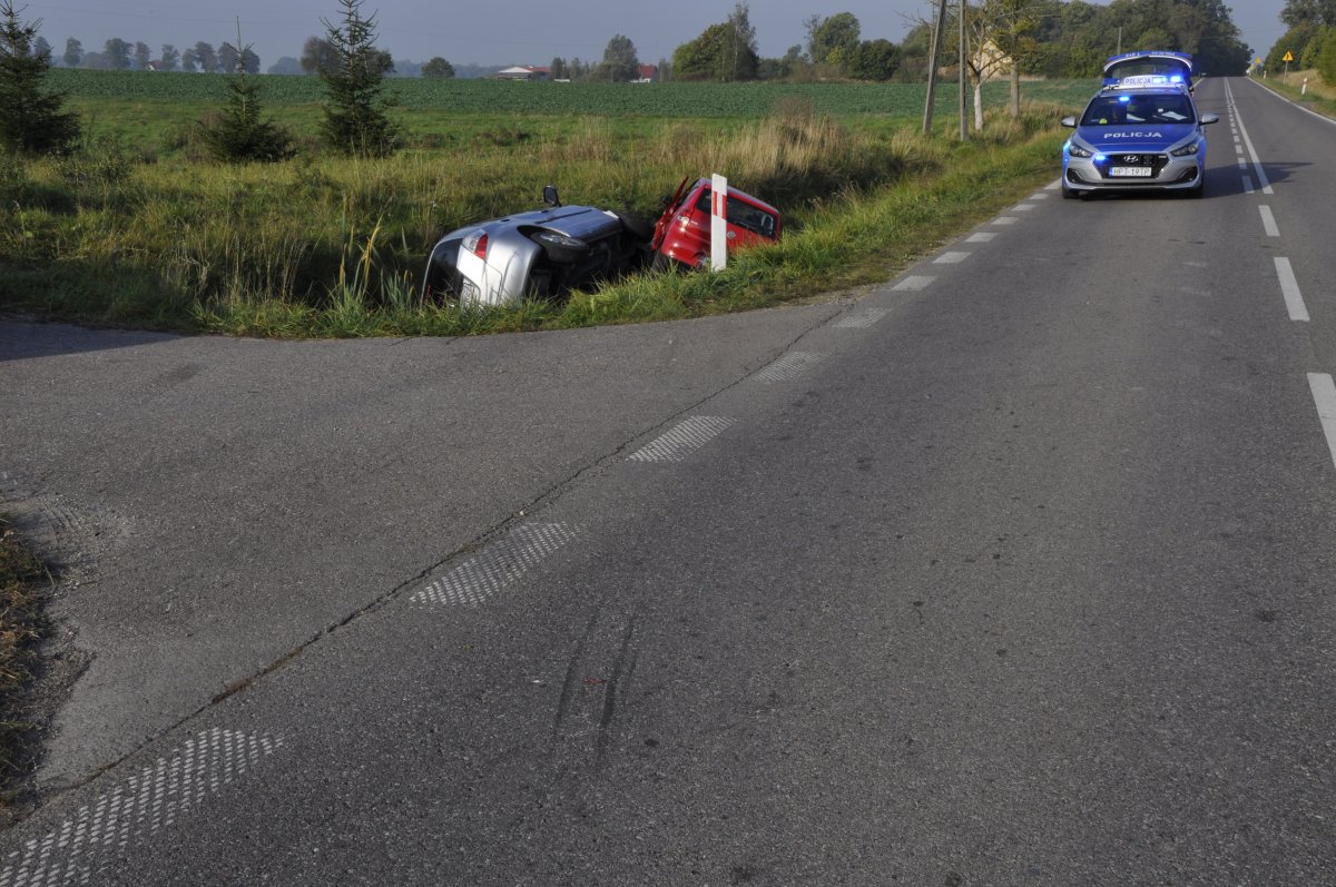 droga W592, po prawej stronie policyjny radiowóz z włączonymi sygnałami świetlnymi, w rowie po lewej stronie czerwony VW i srebrna honda leżą na boku