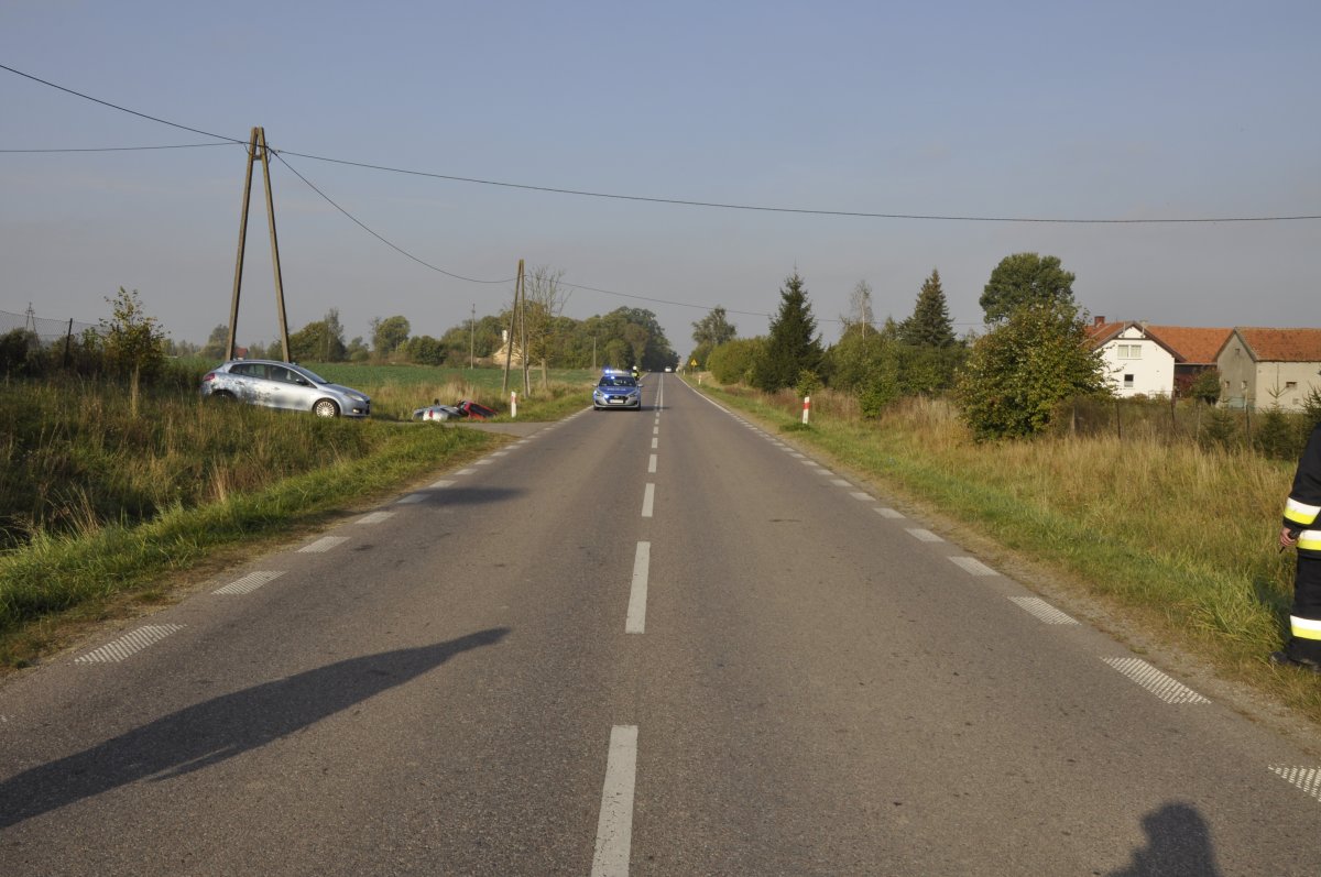 droga W592, po lewej stronie w drodze bocznej nieoznakowany radiowóz, w rowie nieopodal dwa auta, po prawej stronie od rowu stoi oznakowany policyjny radiowóz
