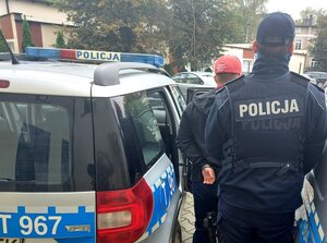 Policjant w umundurowaniu stoi pomiędzy radiowozami z mężczyzną który został zatrzymany
