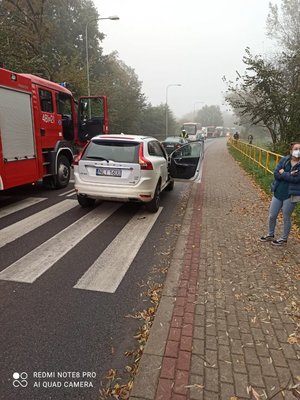 Na zdjęciu widać pojazd stojący na pasach z otwartymi drzwiami od strony pasażera, po prawej stronie pojazdu stoi wóz strażacki
