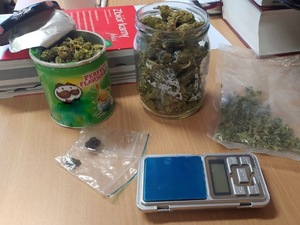 Na zdjęciu słoik z zawartością suszu, pudełko po chipsach z zawartością suszu, 2 woreczki z zawartością, waga, kodeks karny