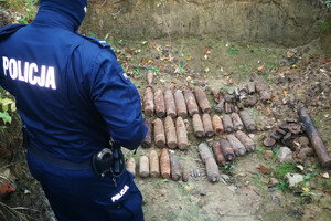 Policjant w miejscu odkrycia niewybuchów. Niewybuchy leżące w ziemi.