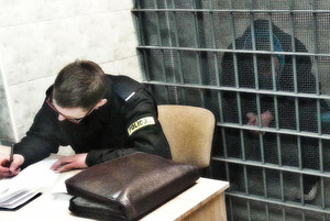 Policjant obok celi, w której siedzi zatrzymany