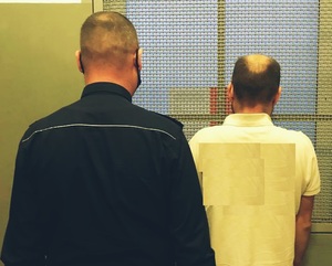 Dwóch mężczyzn stojących tyłem, w tym jeden umundurowany policjant