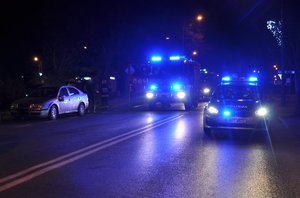 na zdjęciu wieczorową porą wóz strażacki i radiowóz na sygnałach, pojazd osobowy i trzech strażaków
