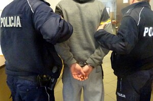 dwóch policjantów prowadzi mężczyznę trzymając pod ręce