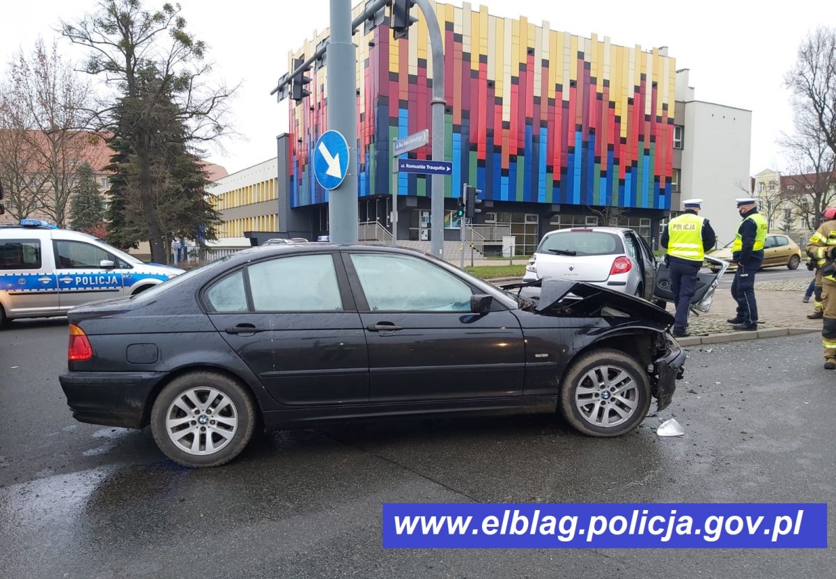 Na zdjęciu 2 rozbite auta osobowe, w oddali zabudowania, radiowóz, 2 policjantów