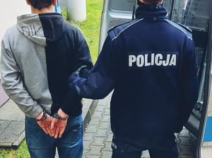 Policjant prowadzi mężczyznę trzymając go pod ręke
