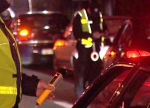 policjant stojący przy pojeździe trzymając w ręku urządzenie do badania alkoholu w tle pojazdy