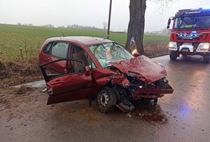 Na zdjęciu rozbite auto stojące w poprzek drogi, w tle samochód straży pożarnej na sygnałach